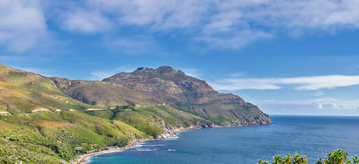 A landscape of a mountainside with an ocean view and blue sky background with a lush, green botanical garden or national park. A scenic environment with rocky and rough terrain in a remote location