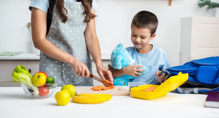 Wall Mural - Young woman making school lunch in the morning. Mother with son preparing school snack or lunch in home kitchen