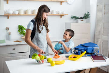 Young woman making school lunch in the morning. Mother with son preparing school snack or lunch in home kitchen