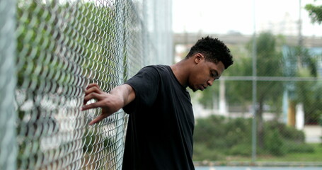 Black guy at basketball court holding into metal fence posing