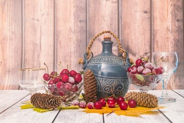 Poster - Vases full of ripe cherries, jug of wine, wine glasses and fir cones lie on wooden table.