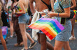 © Dina - Rainbow pride flag closeup. Real people walking at Pride parade with rainbow flag as symbol of Pride month. Queer community march in the street with crowds
