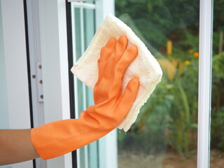 Wall Mural - Woman hand in orange gloves cleaning window with cream rag. Housework concept.