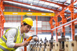 Selective focus at Asian men engineer supervisor, wearing safety equipment. While doing audit for quality and safety control inside of factory area. With blurred background of heavy machine.