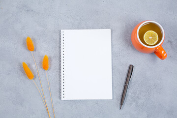 An open blank diary notebook, calendar with dried grass and cup of tea on grey concrete table.