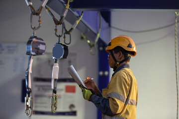 Authorise auditor personal wearing side impact safety helmet standing inspecting an inertial reel fall arrest, fall restraint equipment at training centre attached with structure beam prior used 