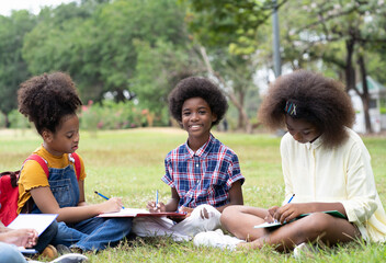 Wall Mural - Group of African American children learning and writing book in the park. Boy and girl sitting and learning outside the classroom. Kids field trips outside. Kids and educational concept