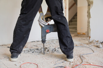 Poster - A man's legs between which he holds a jackhammer scrapes the floor old tiles apartment renovation.