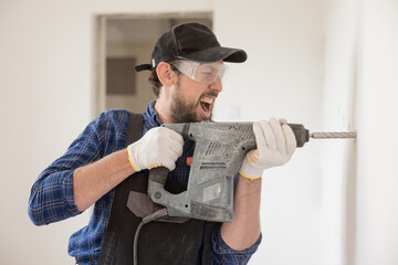 Wall Mural - Portrait of a young man with an electric drill and making a hole in the wall. Interior design and home renovation concept.