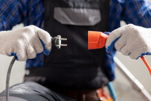 Hands Of A Man Wearing Work Gloves Hold An Extension Cord And Cable Connection Of Two Plugs Plugging The Equipment Into Electricity.
