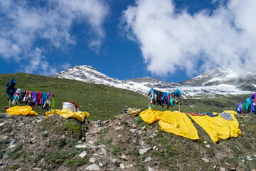 Wall Mural - Snow suit are drying up in the valley with the snow capped mountains in the backdrop. Blue skies with few clouds over mountains and high altitude green meadow can be seen with drying snowsuits.