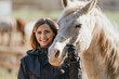 Young woman in black riding jacket standing near white Arabian horse smiling happy, closeup detail