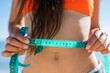 © Sheviakova - a girl in a swimsuit measures her waist with a centimeter for weight loss on the beach