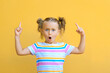Excited surprise little kid girl is attracted by attention pointing finger at copy space. The concept of advertising products , goods and services. Isolated on yellow background