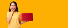 Surprised young asian woman holding red gift box Look at camera with excited face Standing over yellow background Beautiful Asia girl happy smile hold shopping gift box present Using for advertisement