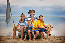 Group Of Happy Children On The Beach In Pirate Costumes With A Helm And A Flag. Funny Happy Kid Outdoor Themed Party. Role-playing Games. Family Vacation In Nature Near The Lake.