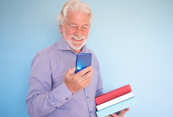 Wall Mural - Smiling bearded senior man holding books in his hand while looking at his cellphone. Senior beautiful teacher going to class