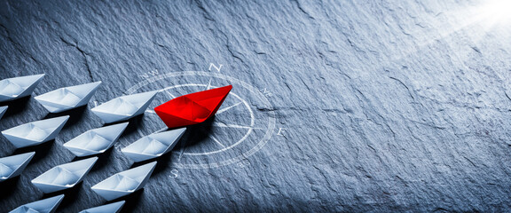 red paper boat on compass leading a fleet of small white boats - business leadership concept