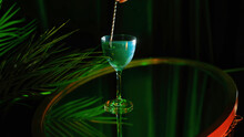 Close up of Aviva green wine with pearl standing on a glass surface table near the plant under green light. Stock footage. Composition in green colors and a hand stiring shining wine with a spoon.