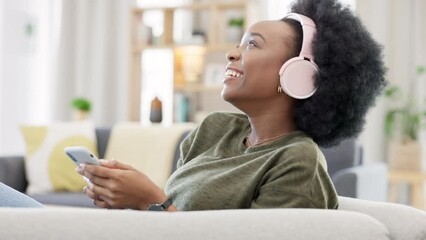 Wall Mural - Woman dancing while listening to music with headphones and using social media to chat to friends online on the couch at home. Carefree black female enjoying her favourite songs and browsing the web