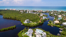Aerial Drone Perspective Of Real Estate In Bonita Springs, Florida With The Bay And A Preserve In The Foreground And The Gulf Of Mexico In The Background Featuring A Blue Sky And Blue Water