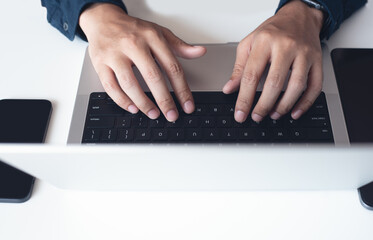 Canvas Print - Business man working on laptop computer, typing on keyboard with digital tablet and mobile phone on white table at office. Man durfing the internet on portable computer