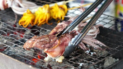 Wall Mural - 4K Slow Motion Video Merchants grilling squids, the most popular seafood street food in Thailand.