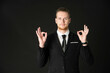 © Arunporn - Portrait of handsome businessman in black suit showing okay symbol hand isolated on black background