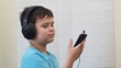 Happy guy, boy at home using a smart phone to listen music with headphones, watching a video, chatting in social networks, playing a game, downloading an application.