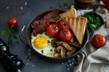 Fried Eggs, Bacon, Tomato And Toasted Bread In A Black Ceramic Pan At Domestic Kitchen