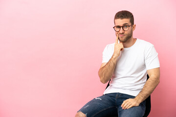 Poster - Young man sitting on a chair over isolated pink background and thinking