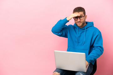 Sticker - Young man sitting on a chair with laptop looking far away with hand to look something