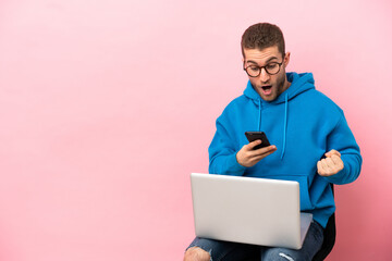 Poster - Young man sitting on a chair with laptop surprised and sending a message