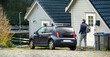 © scharfsinn86 - A man with a backpack next to charging electric car near a country house