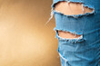 Leg in a torn jeans closeup, tattered jeans on a light brown background with a place for your text