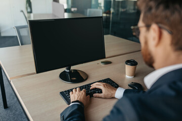 Poster - Unrecognizable businessman using computer with empty screen at office, sitting at workplace, offering space for mockup