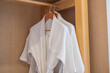 White clean bathrobe hanging in wooden wardrobe at luxury hotel or home. Relax and travel concept