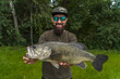 Bass fishing. Large bass fish in hands of pleased bearded fisherman. Largemouth perch at pond