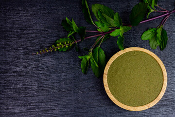 Holy basil powder on wooden bowl with branch on black wooden background, top view. Holy basil leaf are useful herbs and food ingredient has a spicy flavor.