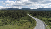 Aerial Of The Empty Road Going Through Forest, Summer Nature Landscape. Scene. Flying Above The Highway Through The Green Spruce Forest On Blue Cloudy Sky Background.