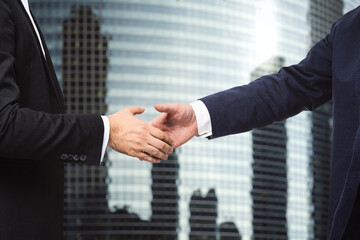 Handshake of two businessmen on the background of office building windows, partnership concept, close up