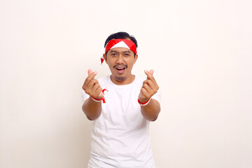 Asian man standing with love finger gesture. Celebrating indonesian independence day.