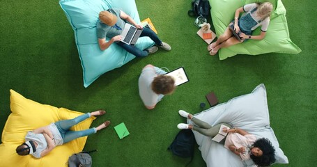 Aufkleber - Aerial view of designers using smart technology while relaxing on bean bags in a casual and colorful office workspace. Student riding a hoverboard in a trendy, modern and bright library from above.