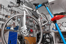White Bicycle Is Fixed On A Blue Holder For Preventive Inspection And Repair In The Service Center. In The Garage Workshop, The Bike Is Repaired And Serviced Against The Background Of Wall With Tools