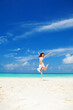 Happy young woman jumping on the beach. White sand, blue cloudy sky and crystal sea of tropical beach. Vacation. Ocean beach relax, travel to islands. Happy lifestyle.