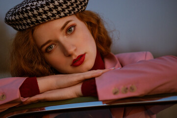 Fashionable elegant redhead freckled woman with dark red lips makeup, wearing houndstooth print beret, posing near vintage car. Outdoor autumn fashion close up portrait. Film grain effect
