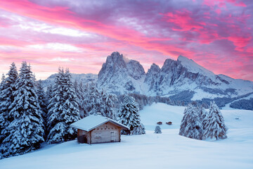 Wall Mural - Picturesque landscape with small wooden log cabin on meadow Alpe di Siusi on sunrise time. Seiser Alm, Dolomites, Italy. Snowy hills with orange larch and Sassolungo and Langkofel mountains group