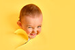 The cunning face of a child looks out of a hole in the studio yellow background. An insidious baby boy peeks through a torn paper background, copy space. Kid age one year