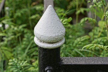 Sticker - one sharp black white metal rod in an iron decorative fence on the street against the background of green grass