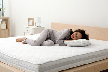 Poster - Happy young African American woman on bed with comfortable mattress and pillow at home